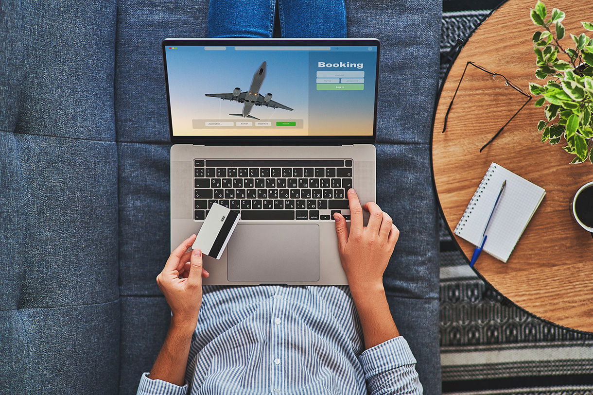 A top-down view of someone booking travel on a laptop and holding a credit card.